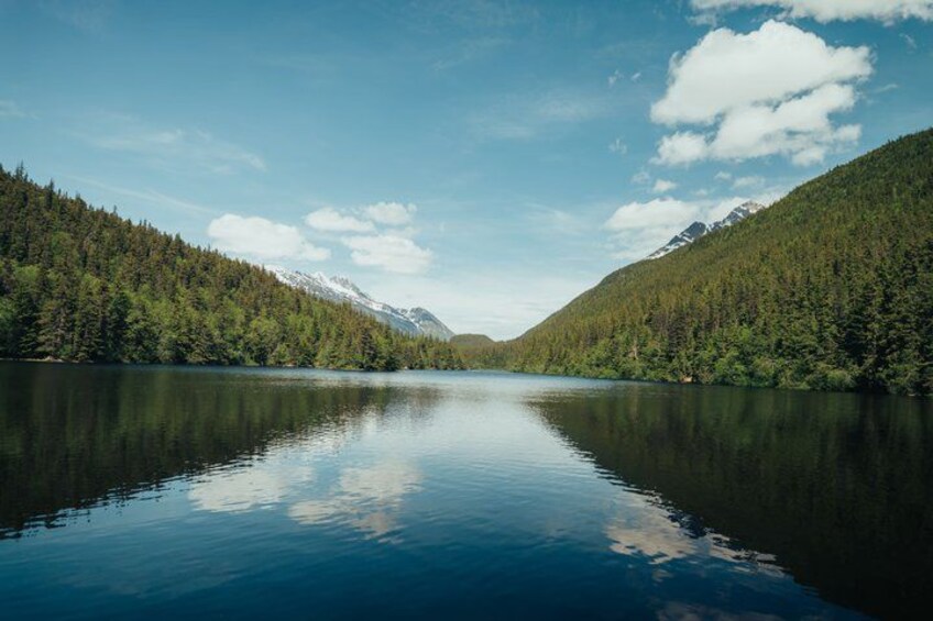 A calm lake surrounded by forested mountains under a clear sky. 4