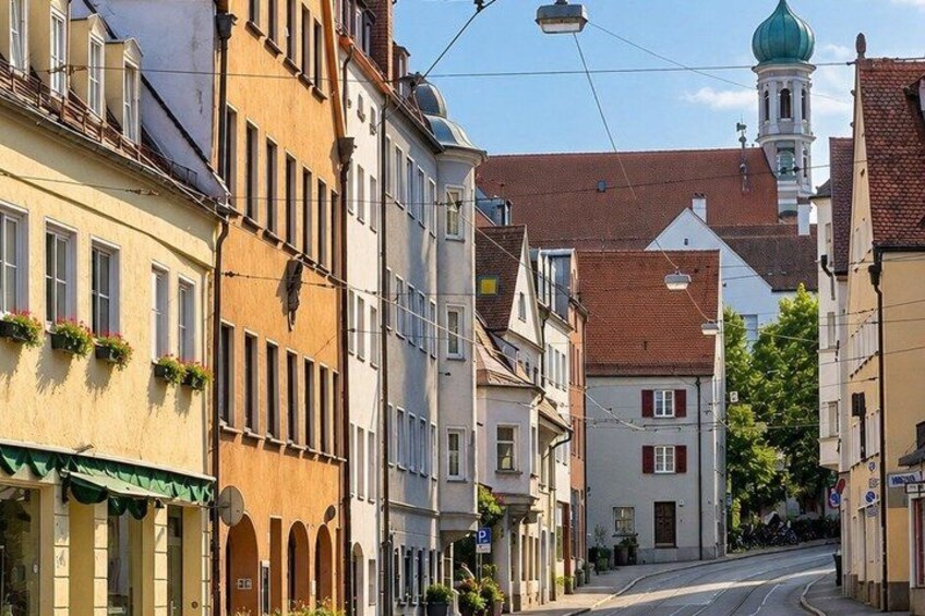 A street lined with historic buildings, a church with a green dome, and a tram track. 3