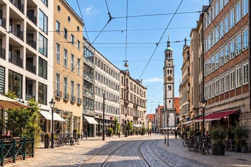 A cobblestone street with tram tracks, historic buildings, and a clock tower. 4