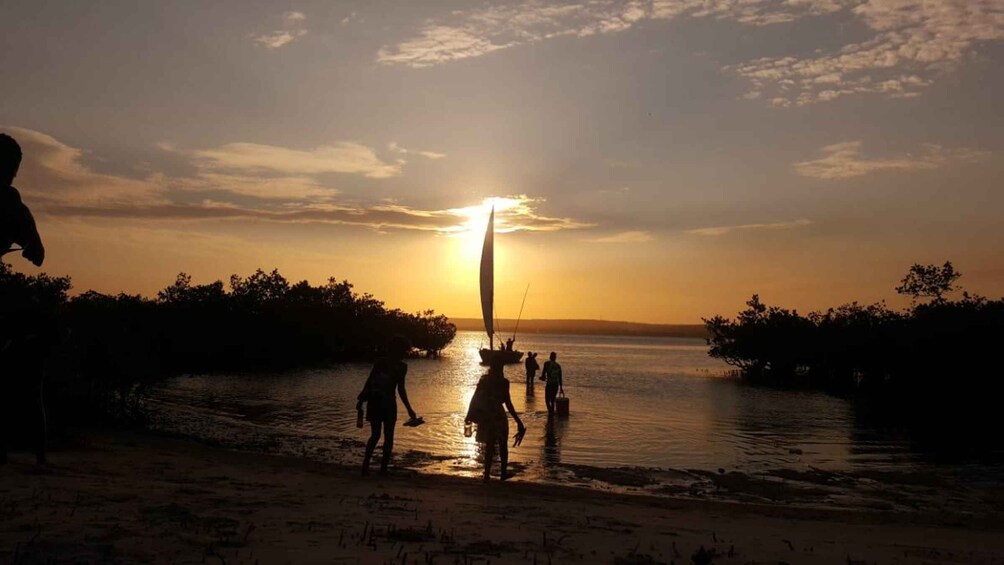 A sunset over a body of water with silhouettes of people and a sailboat. 1