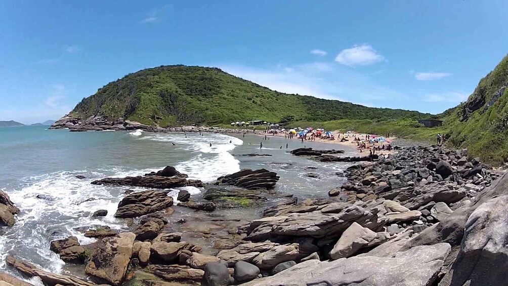 Una playa rocosa con olas, una colina boscosa y gente en la orilla. 1