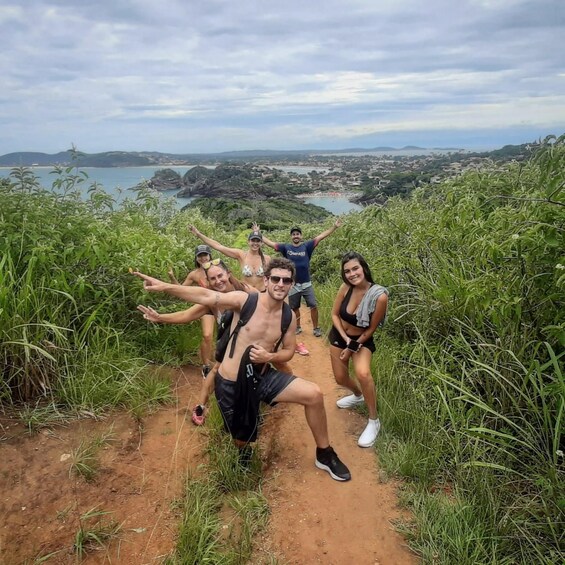 Un grupo de personas posando en un sendero de tierra con una vista panorámica de un pueblo costero y colinas al fondo. 2