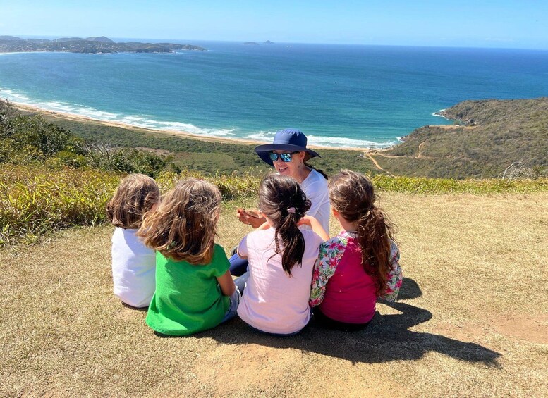 Un grupo de personas sentadas en una colina cubierta de hierba, con vistas a un paisaje costero y una vista despejada del océano y colinas distantes. 4