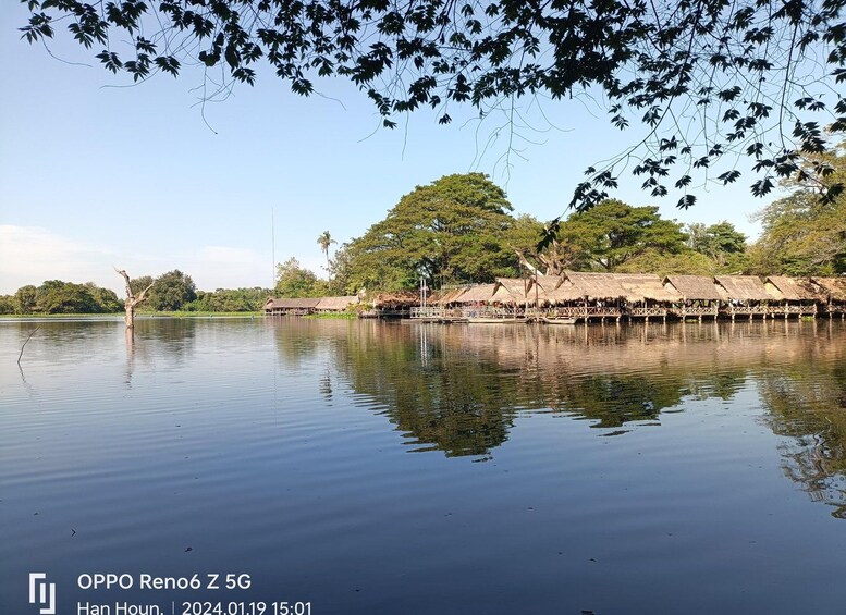 A calm lake with a thatched-roof structure on stilts, surrounded by lush greenery and trees. 5