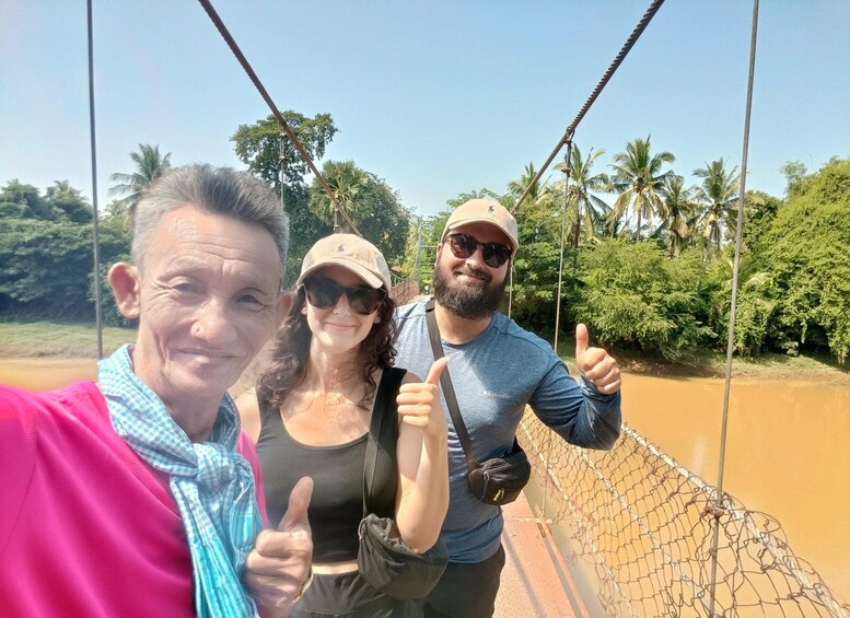 Three people on a suspension bridge with a river and greenery in the background. 3