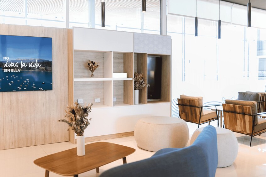 A modern interior with a wooden wall, a mounted TV, and a seating area with a round ottoman and chairs. 2