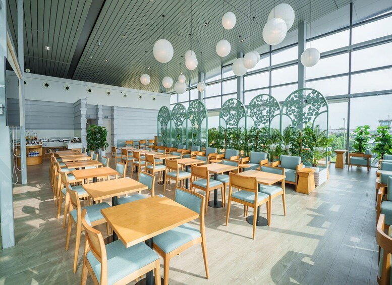 A spacious indoor area with wooden tables and chairs, large windows, and hanging spherical lights. 1