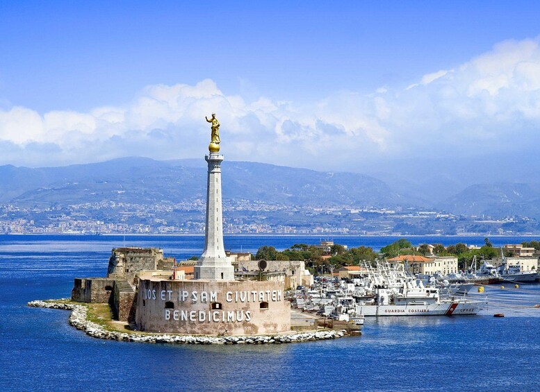 A coastal cityscape with a prominent monument inscribed with 'VOS ET IPSUM CIVITATEM BENEDICIMUS' surrounded by a harbor with boats and a distant mountain range. 1
