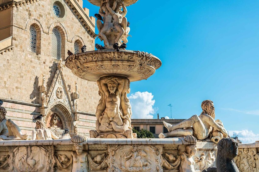 A detailed fountain with sculptures, set against a historic building with arched windows and intricate carvings. 3