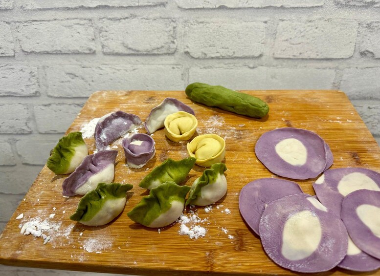 A wooden cutting board with dumplings, some cut open to reveal a filling, and a green vegetable, possibly a cucumber, on a white brick wall background. 4