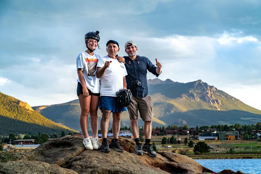 Three people standing on a rock with a mountainous landscape in the background. 1