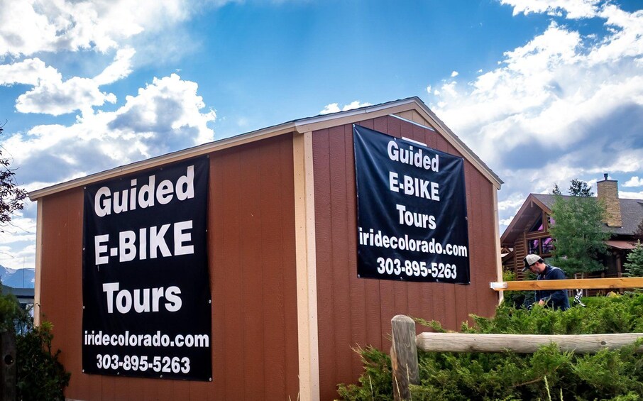 A wooden building with two black banners advertising guided e-bike tours. 2