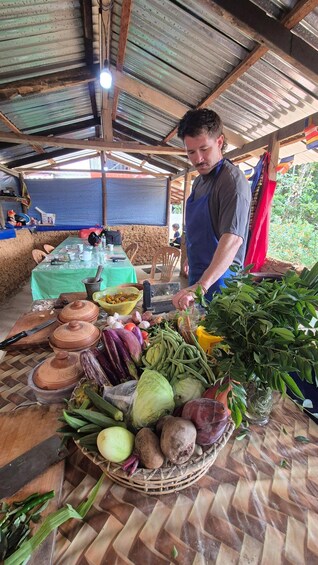 Une personne prépare des aliments à base de légumes sur une table, en utilisant des ustensiles de cuisine, et se trouve sous un toit en tôle ondulée. 5