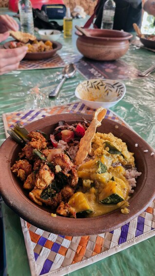 Un plat composé de riz, de poulet et de légumes, servi dans un pot en argile sur une table recouverte d’un set de table en fibres tressées. 3