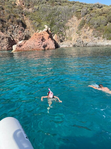 Nadador en un mar azul cristalino con acantilados rocosos al fondo. 3