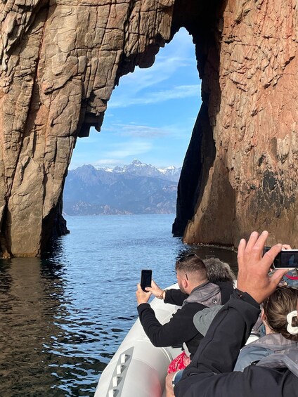 Un grupo de personas en un bote cerca de una formación rocosa con forma de arco, con un paisaje montañoso al fondo. 4