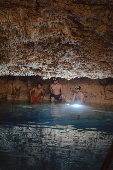 Three people sitting in a cave with a water pool. 4