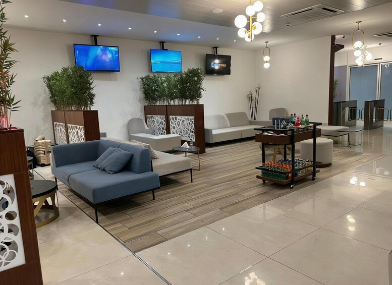A modern living room with a blue sofa, a white couch, and a coffee table. There are two wall-mounted TVs displaying different scenes. 3