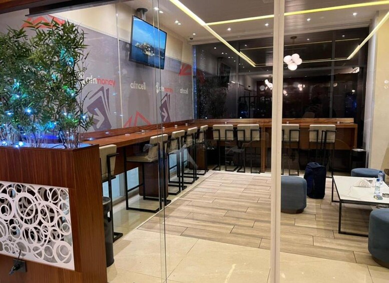 A modern indoor seating area with wooden tables and chairs, a decorative plant, and a television screen on the wall. 2