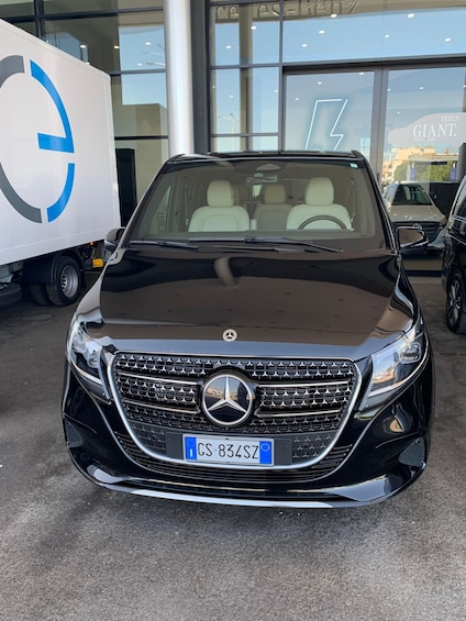 Un SUV Mercedes-Benz negro estacionado en una sala de exposición, con una camioneta blanca grande al fondo. 5