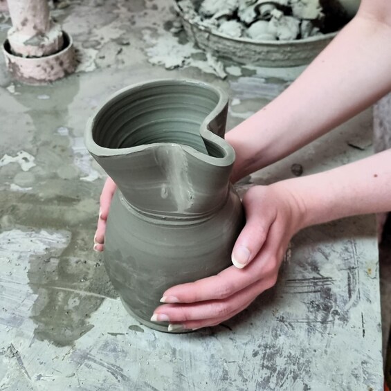 A person shaping a green ceramic jug on a workbench. 1