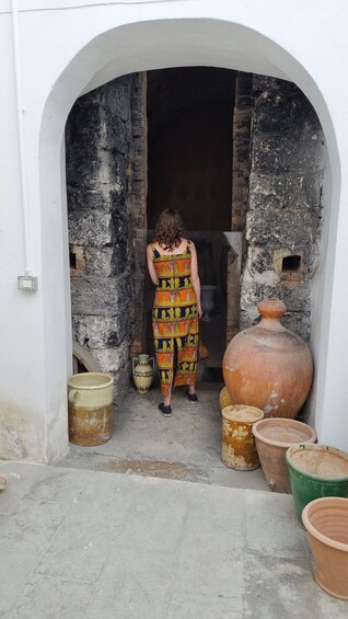A person exiting through an arched doorway, surrounded by large clay pots. 4