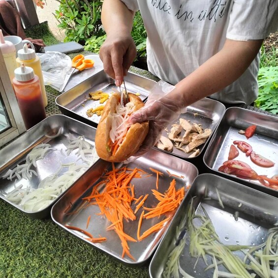 A person preparing a sandwich with various ingredients on a metal tray. 2