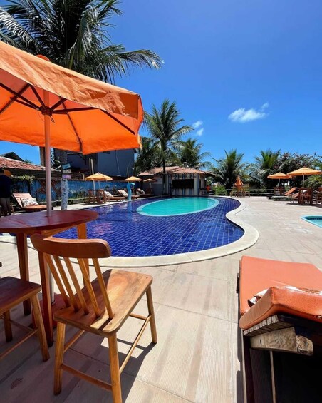 Una piscina con baldosas azules, rodeada de sillas de madera y sombrillas naranjas. 2