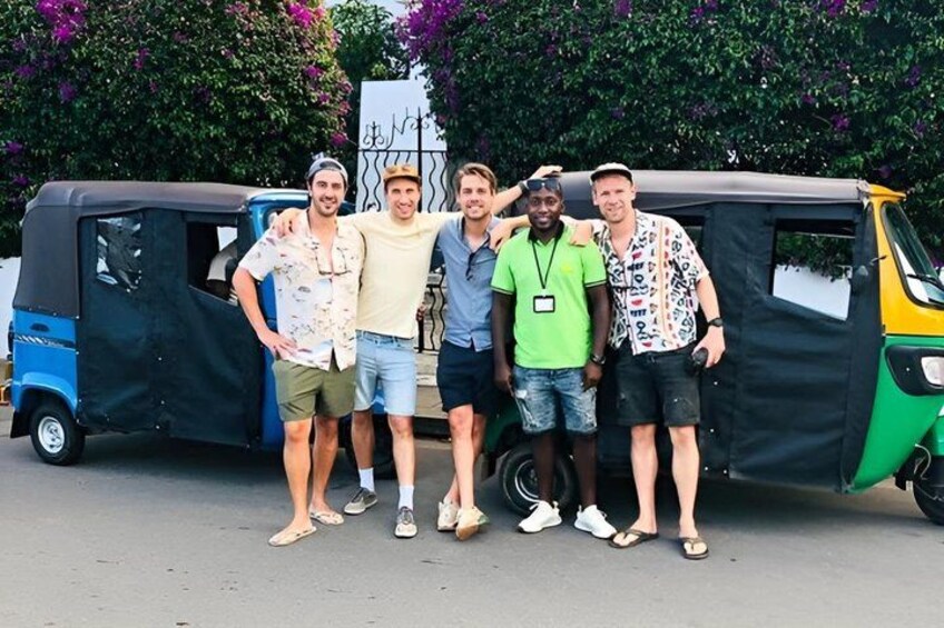 Five people standing in front of a covered vehicle with a sign in the background. 1