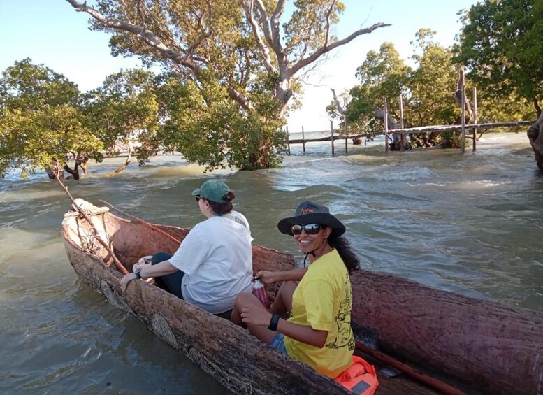 Two people in a wooden boat on a calm river surrounded by trees. 1