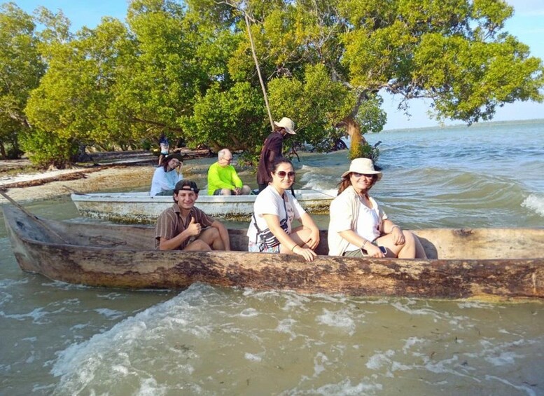 A group of people in a wooden boat on a calm body of water, surrounded by lush green trees. 4