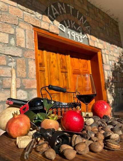 A wooden table with a wine bottle, wine glass, pomegranate, apples, and corks. 4