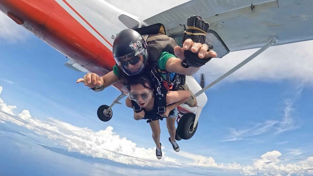 Two people skydiving with a parachute, pointing towards the camera. 1