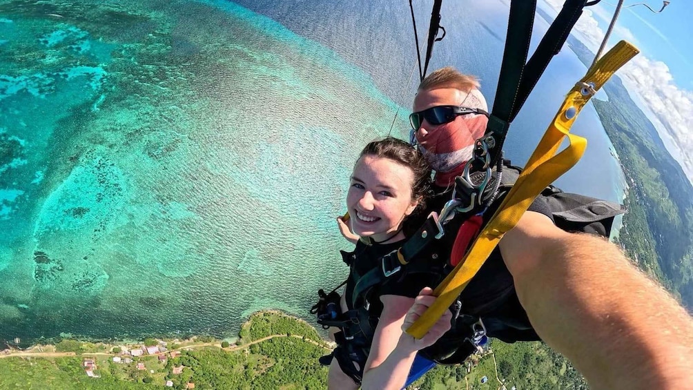 A person taking a selfie while skydiving over a turquoise ocean. 3