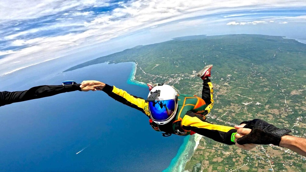 Two people skydiving with a parachute, holding hands, over a coastal landscape with a clear sky. 4