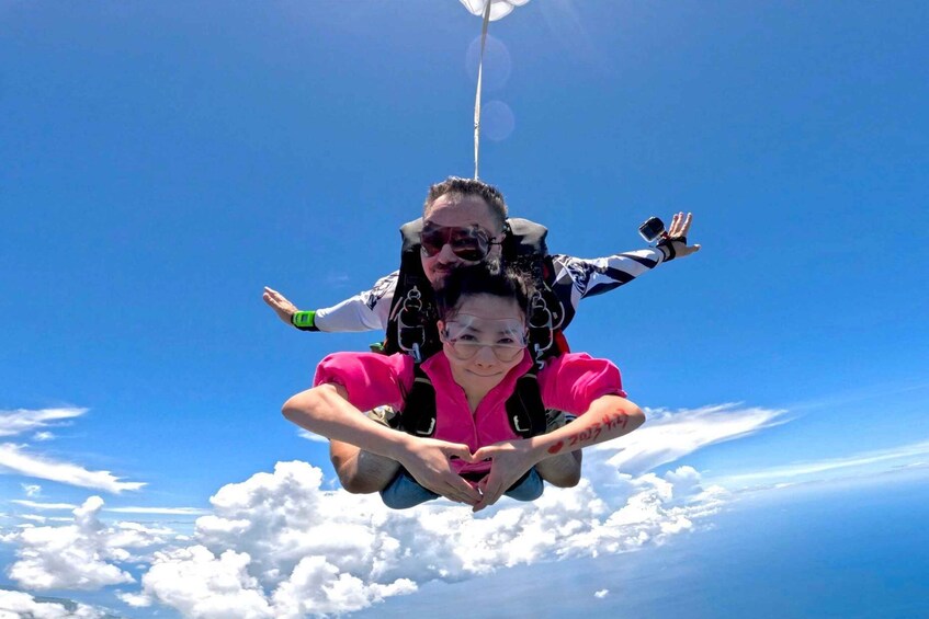 A person in a harness with a child, both in freefall with a parachute above. 2