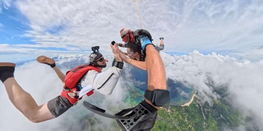 Two people skydiving with a parachute, surrounded by clouds and a landscape below. 5