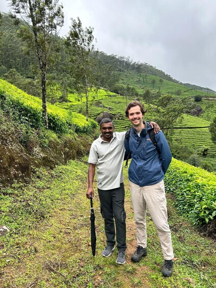 Two people standing in a hilly tea plantation with lush greenery and terraced fields. 4