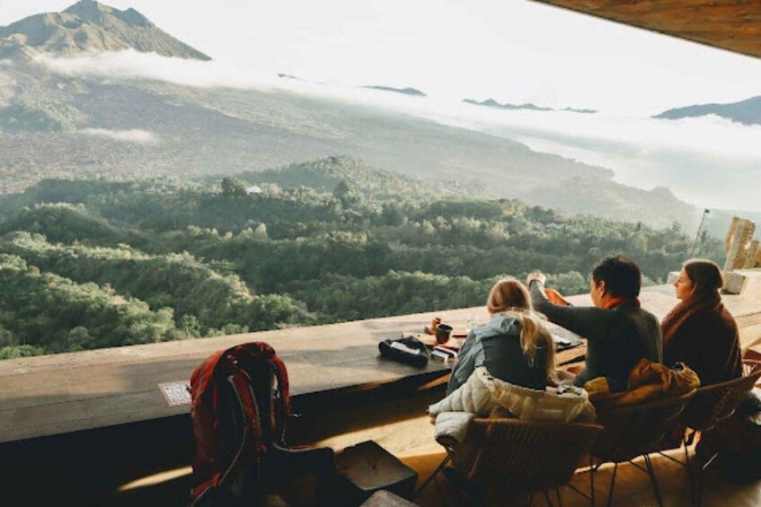 A couple and a child overlooking a mountainous landscape with a forested valley and mist-covered peaks. 4