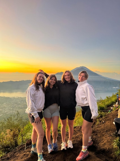 Four people standing on a mountain ridge with a sunset and a volcano in the background. 5