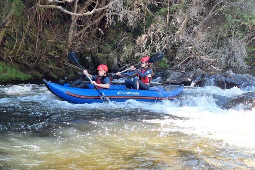 Two people kayaking on a river surrounded by trees. 1