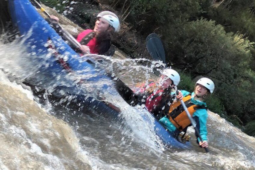 Two people in a blue raft navigating a river with rapids. 2