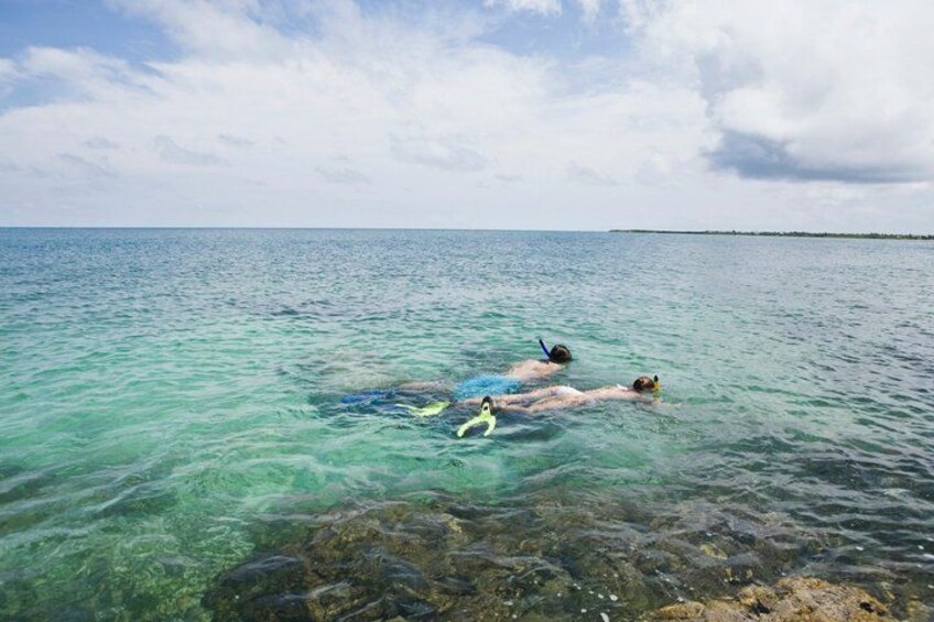 Two people swimming in clear turquoise water with rocks at the bottom. 3
