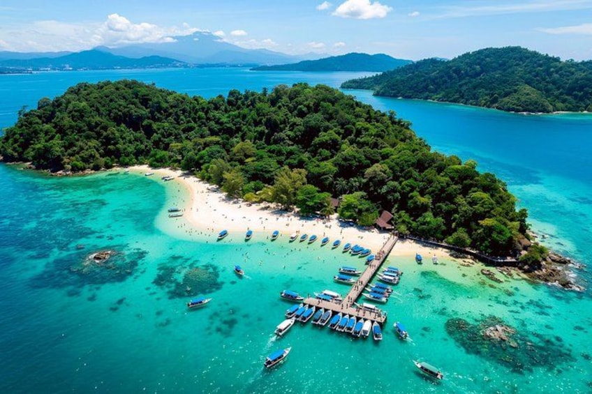 An island with a beach, boats, and clear turquoise waters. 1