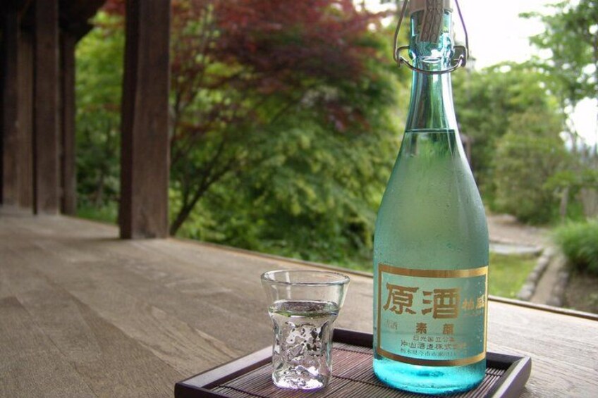 A bottle of sake and a small glass on a wooden table outdoors. 4