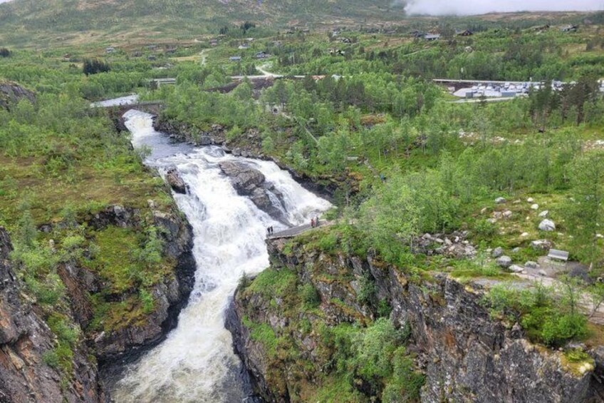 A waterfall cascading through a valley with surrounding greenery and a distant settlement. 5