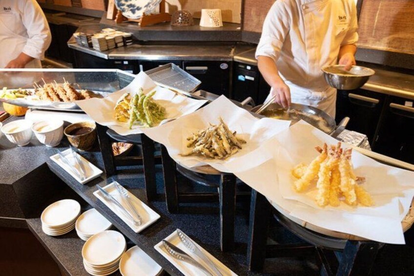 A kitchen with chefs preparing food, including tempura and other dishes. 3