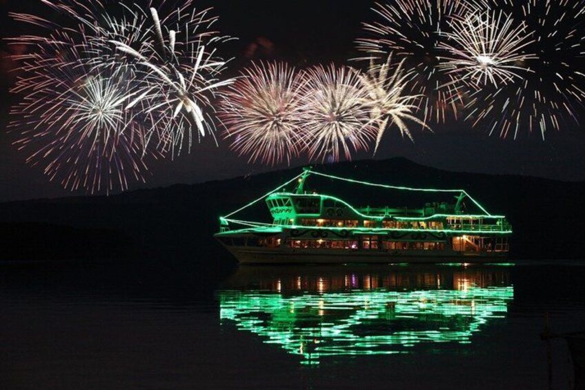 A boat with green lights reflecting on water, fireworks in the sky, and a mountain in the background. 1