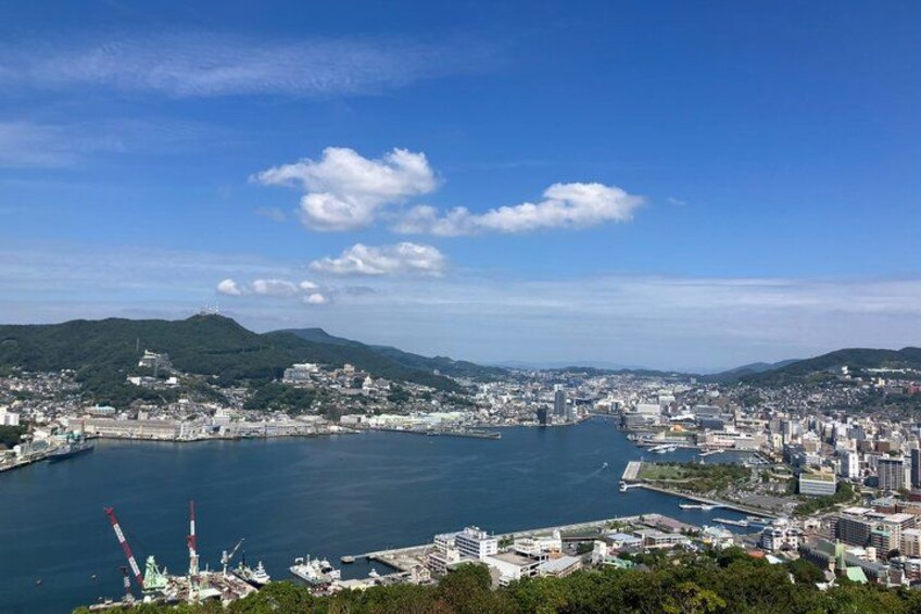 A coastal cityscape with a large body of water, a prominent hill with a structure on top, and a dense urban area with buildings and infrastructure. 3