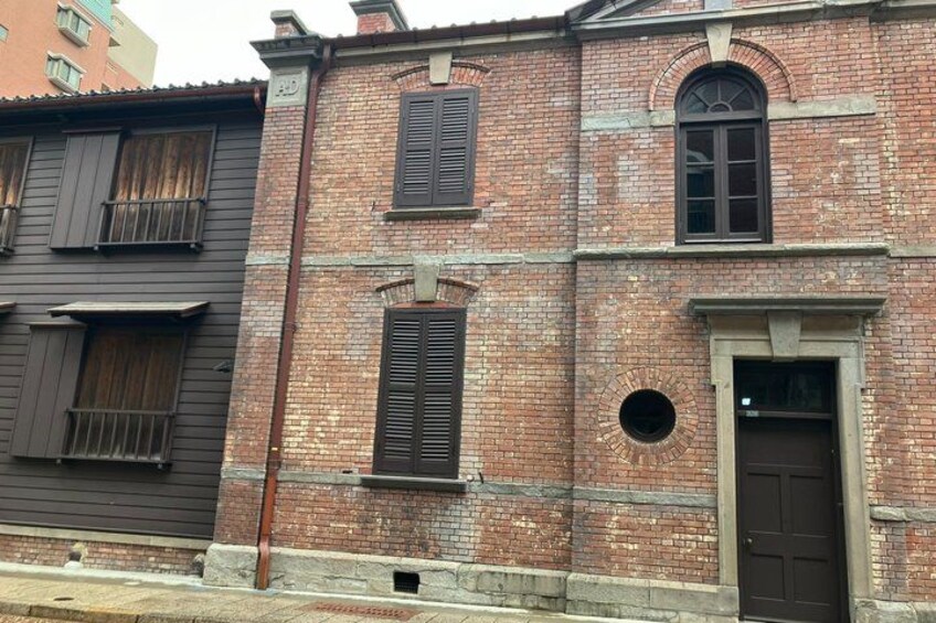 A brick building with a brown door and windows with shutters. 2